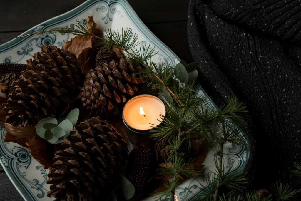 A candle lit with cozy christmas decorations around it