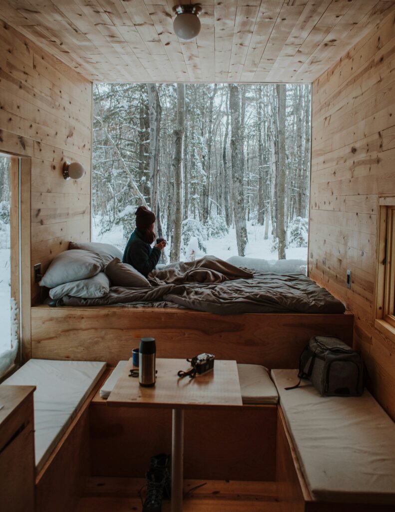 a woman in bed looking out the window into the woods, digitally detoxing in her cabin