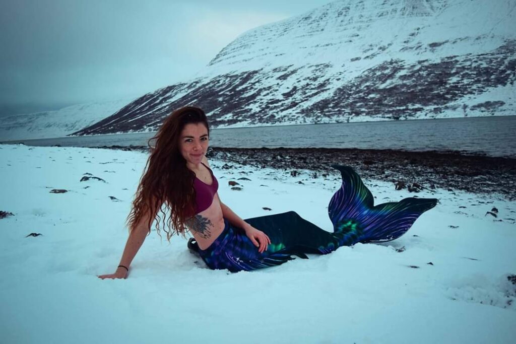 Elaina with a mermaid tail in the snow practicing cold therapy