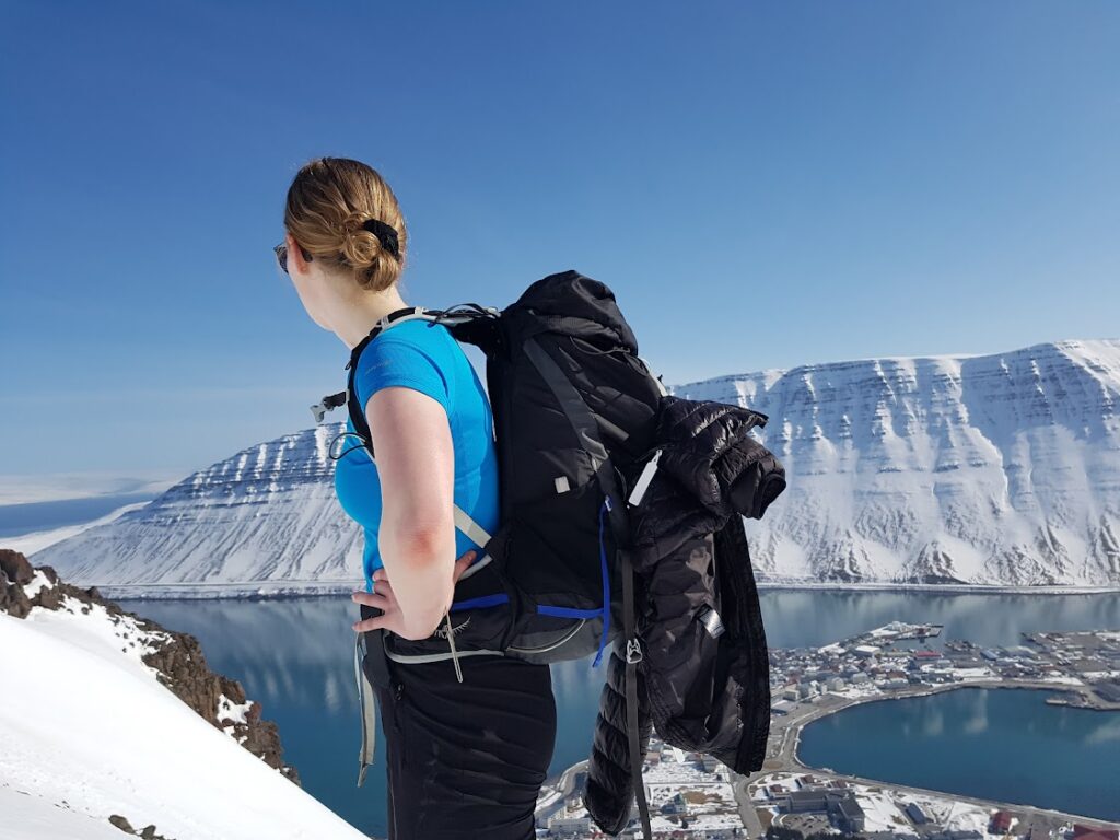 A woman hiking a snowy mountain looking down on the fjord