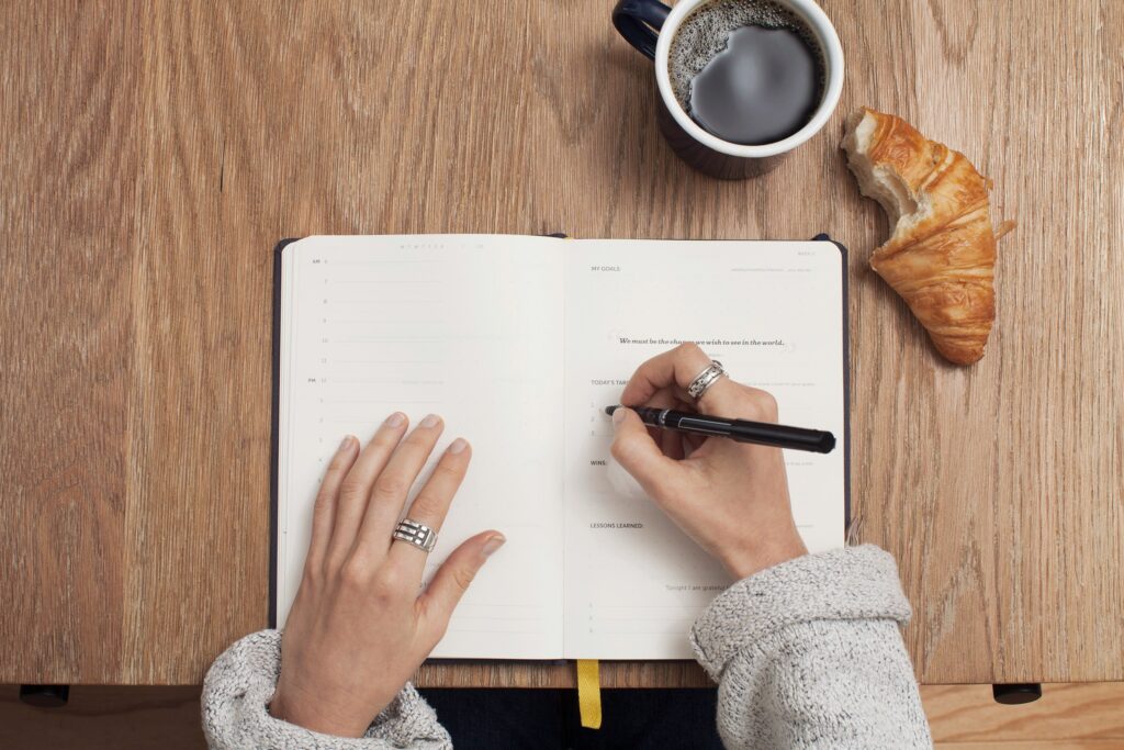 A woman journaling to set goals for the new year with a coffee and croissant