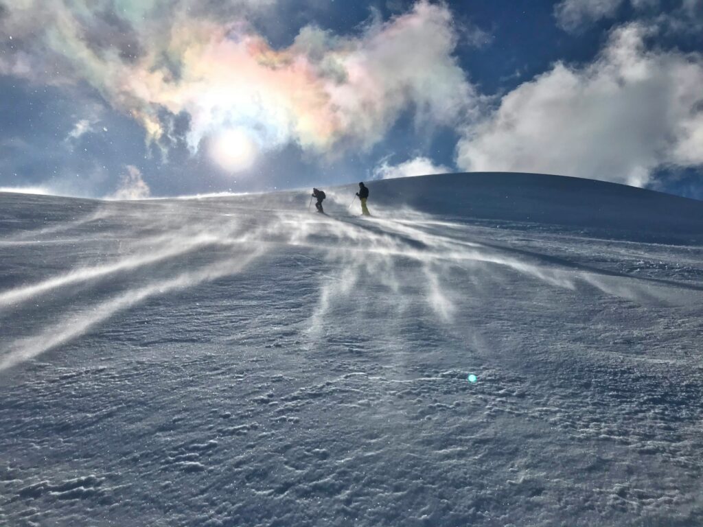 Two people walking on a snowy mountain in the sun 