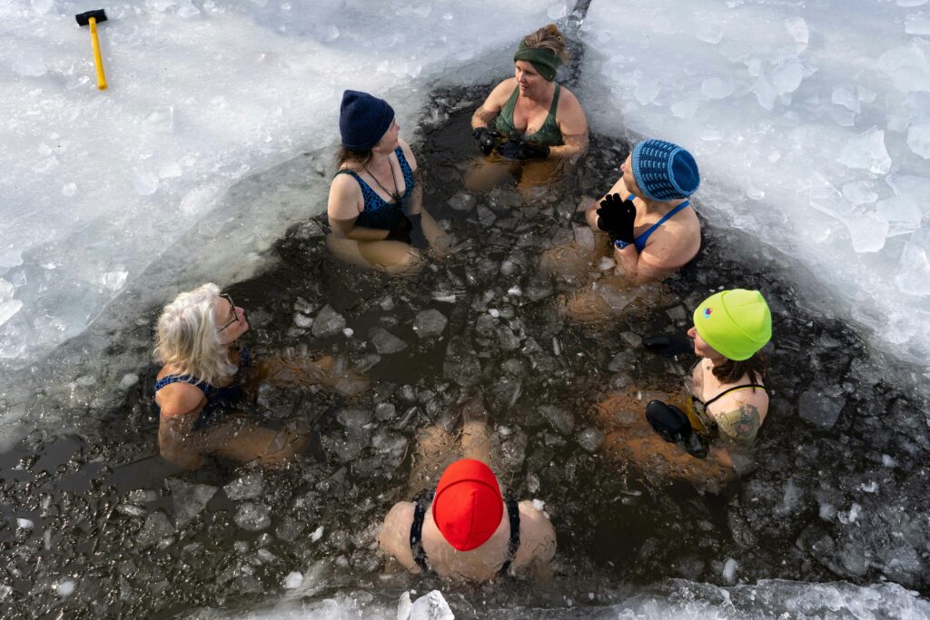 women sitting together doing an cold plunge in a frozen lake