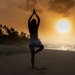 A girl doing a yoga pose on the beach at sunset