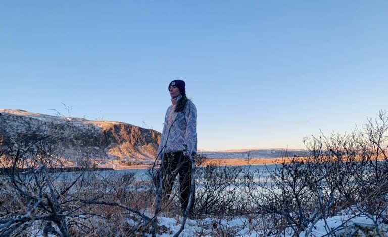 Elaina standing by a lake at sunrise in the winter, looking at the view with content. This signifies peace of mind from breathwork.