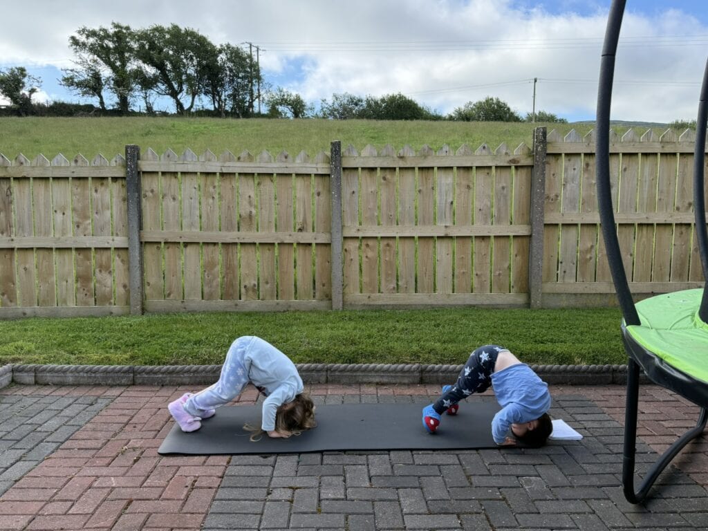 Learning breathwork for nervous system regulation with two kids playing outside on a yoga mat, doing downward dog