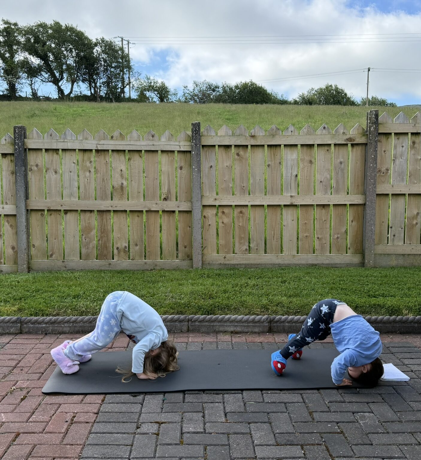 Learning breathwork for nervous system regulation with two kids playing outside on a yoga mat, doing downward dog